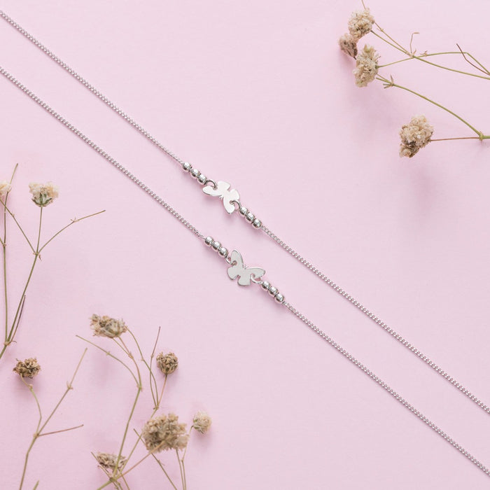 Two butterfly 925 Sterling Silver anklets for women. Minimalist jewellery on a pink floral background – Zavya
