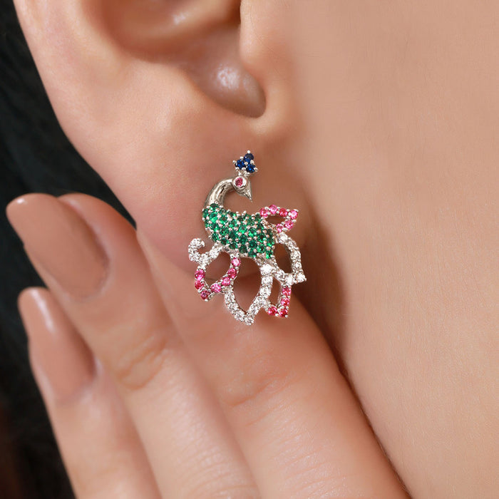 Woman wearing a 925 Sterling Silver peacock stud earring with green and pink stones. Women's jewelry – Zavya