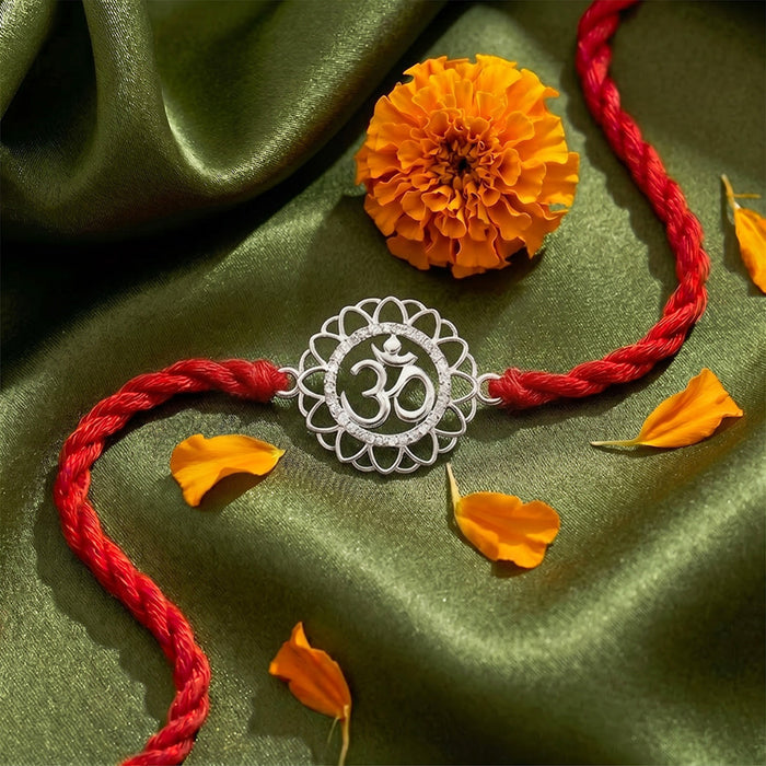 A silver Om Rakhi on a red braided string,