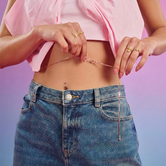 Woman with pink top adjusting a rose gold 925 Sterling Silver waist chain jewellery above blue jeans – Zavya