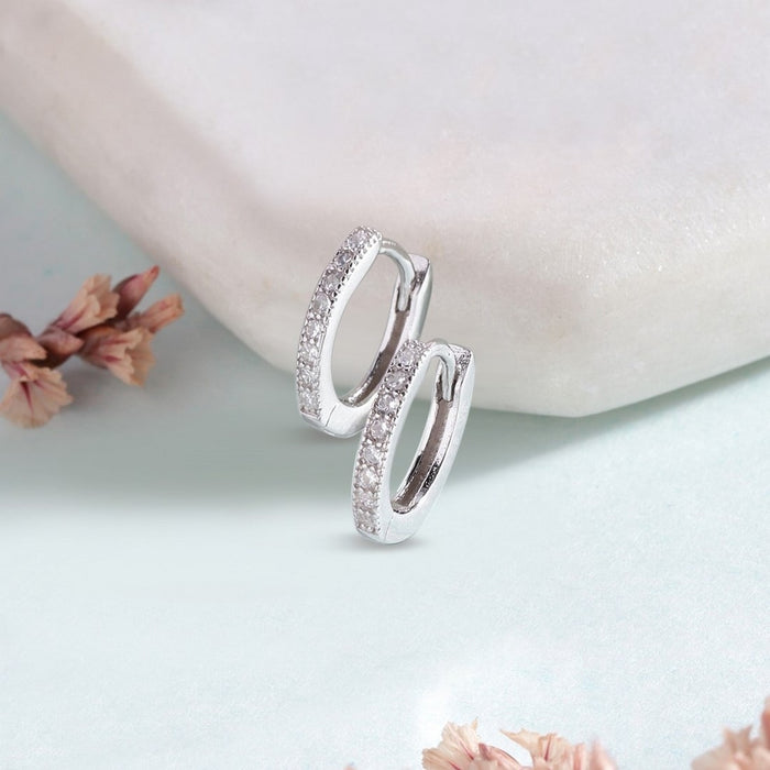 Women's 925 Sterling Silver studded hoop earrings resting against a white stone with pink flowers – Zavya