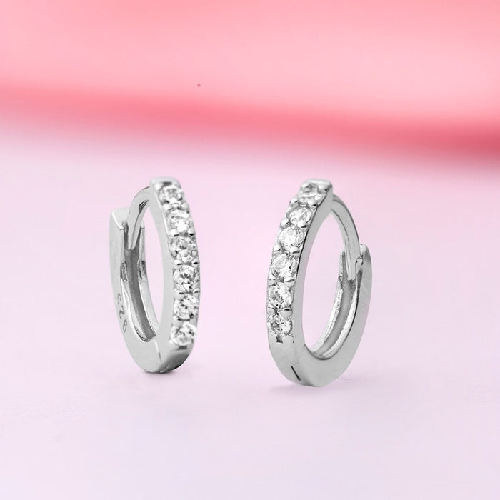 Women's 925 Sterling Silver huggie hoop earrings with sparkling stones on a pink background – Zavya
